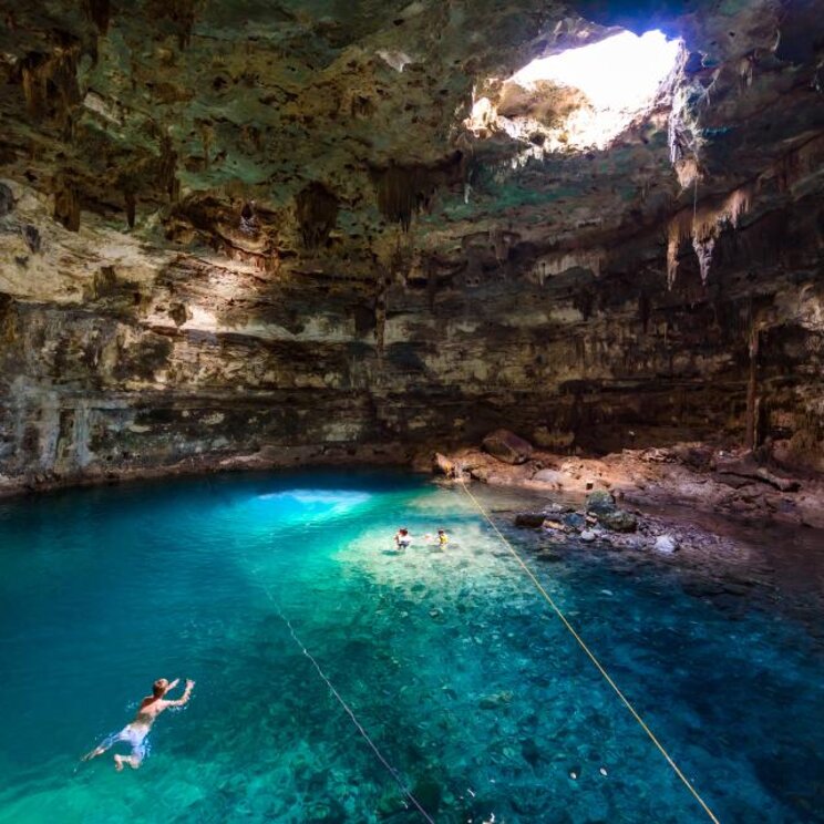 Leute schwimmen im türkisen Wasser einer Cenote in Mexiko