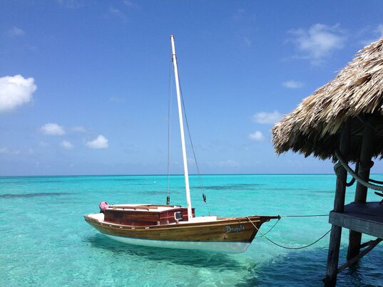 Segelboot am Steg im türkisblauen Wasser des Glover’s Reef Atolls in Belize unter strahlend blauem Himmel.