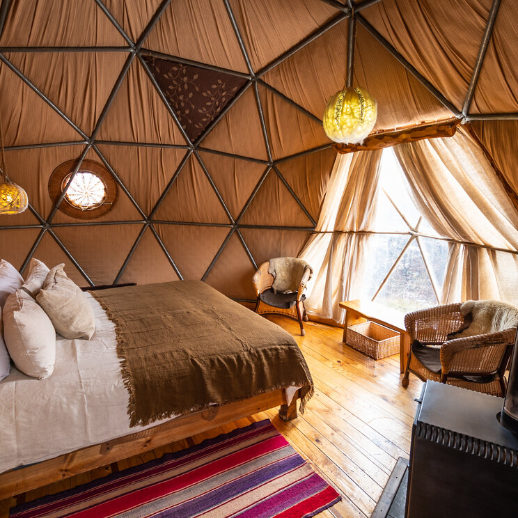 Schlafbereich in einem Suite Dome mit Doppelbett, Holzofen und Korbsesseln im EcoCamp Patagonia, Chile.