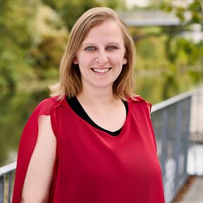 Judith Seeck, Mitarbeiterin bei Gateway Lateinamerika, steht lächelnd auf einer Brücke mit grünem Flussufer im Hintergrund.