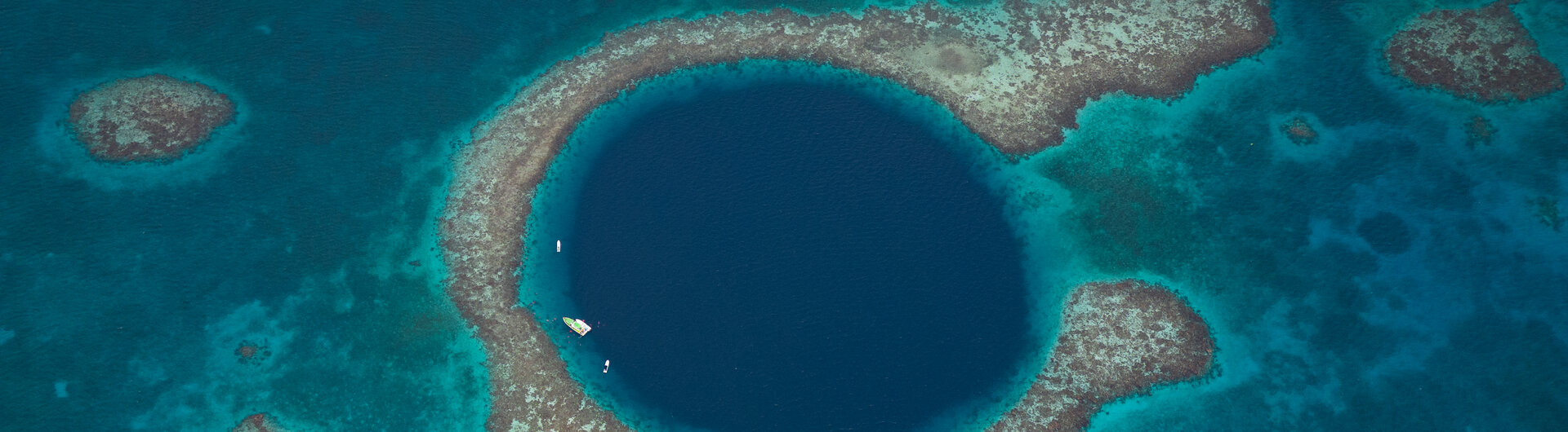 Luftaufnahme des kreisrunden, dunkelblauen Great Blue Hole inmitten von Korallenriffen in Belize.