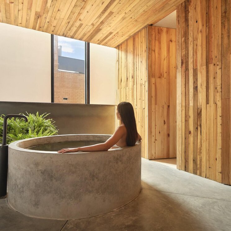 Frau in einer runden Betonbadewanne im Wellnessbereich des Hotel Otro mit Holzwaenden in Oaxaca.