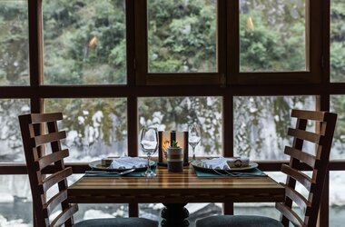 Zweier-Tisch an einem großen Fenster mit Blick auf eine bewachsene Felswand im Restaurant in Peru.