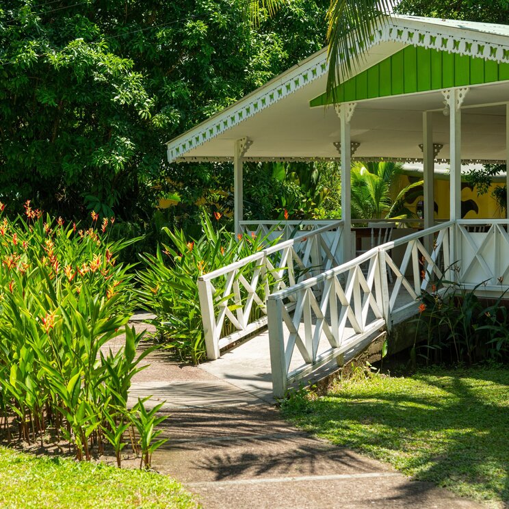 Weißer, überdachter Holzpavillon mit einer kleinen Brücke im grünen Garten der Laguna Lodge.
