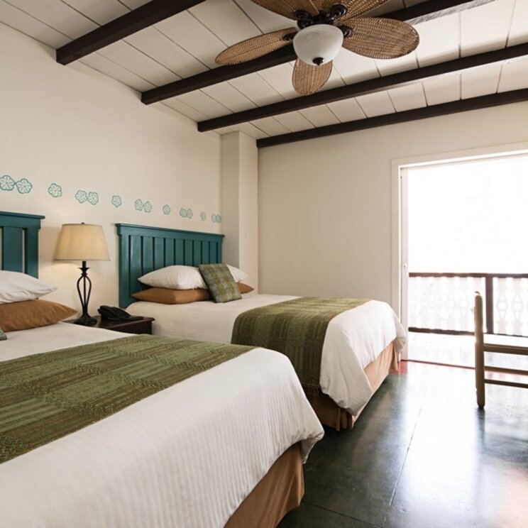 Junior Suite mit zwei Betten, gruenen Laeufern, Deckenventilator und dunklem Holzschrank im Hotel Isla de Flores.