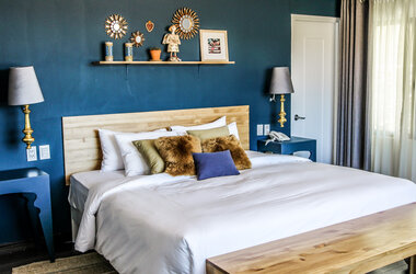 Grosses Doppelbett vor blauer Wand mit goldenen Wandspiegeln und dekorativem Regal im Hotel Tariq.