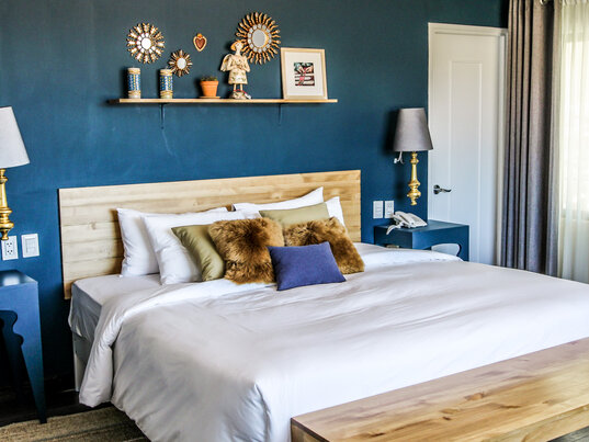 Grosses Doppelbett vor blauer Wand mit goldenen Wandspiegeln und dekorativem Regal im Hotel Tariq.