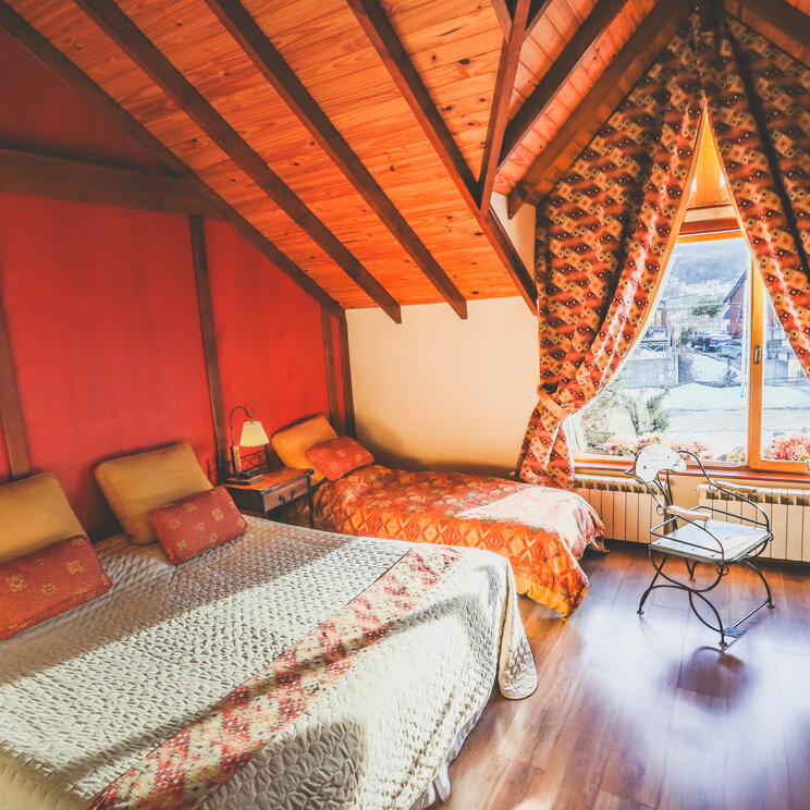 Gemütliches Standard-Dreibettzimmer im Hotel Tierra de Leyendas in Ushuaia mit Holzdecke, Doppel- und Einzelbett.