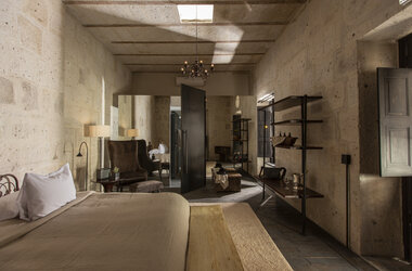 Modernes Suite-Interieur mit Steingewaenden, dunklem Holzregal und Blick auf das Bett im CIRQA Hotel Arequipa.