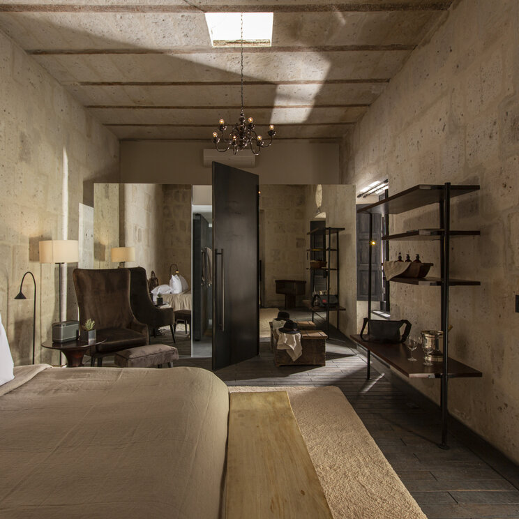 Modernes Suite-Interieur mit Steingewaenden, dunklem Holzregal und Blick auf das Bett im CIRQA Hotel Arequipa.