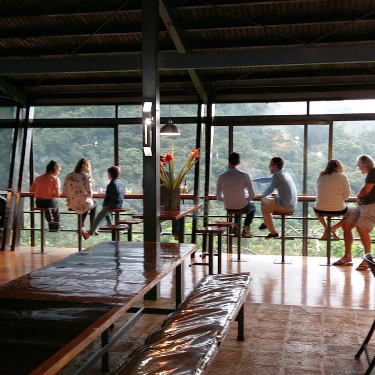 Gaeste sitzen auf Barhockern an einer Panoramafensterfront der Celeste Mountain Lodge und blicken in die Natur.