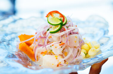 Peruanisches Ceviche mit Fisch, roten Zwiebeln, Limette und Süßkartoffel auf Glasteller.