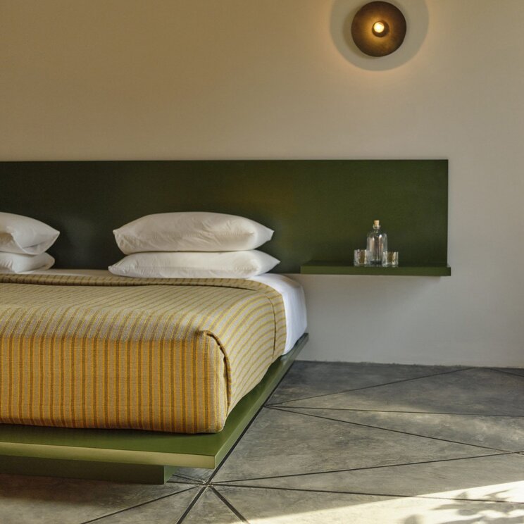 Modernes Bett mit gruenem Kopfteil und gestreifter Tagesdecke im Hotel Otro in Oaxaca, Mexiko.