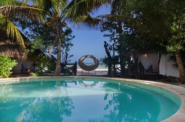 Blick über einen runden Pool auf eine Skulptur und das Meer auf Holbox.