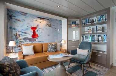 Gemütliche Bibliotheksecke auf der Ocean Albatros mit Ledersofa, Plüschsesseln, Büchern zur Antarktis und einer großen Landkarte der Antarktis an der Wand