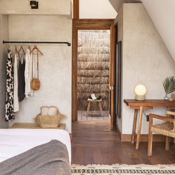 Zimmer im Hotel Our Habitas Bacalar mit stilvoller Einrichtung, Holzboden und Zugang zu einem privaten Außenbereich mit Palmenwand.