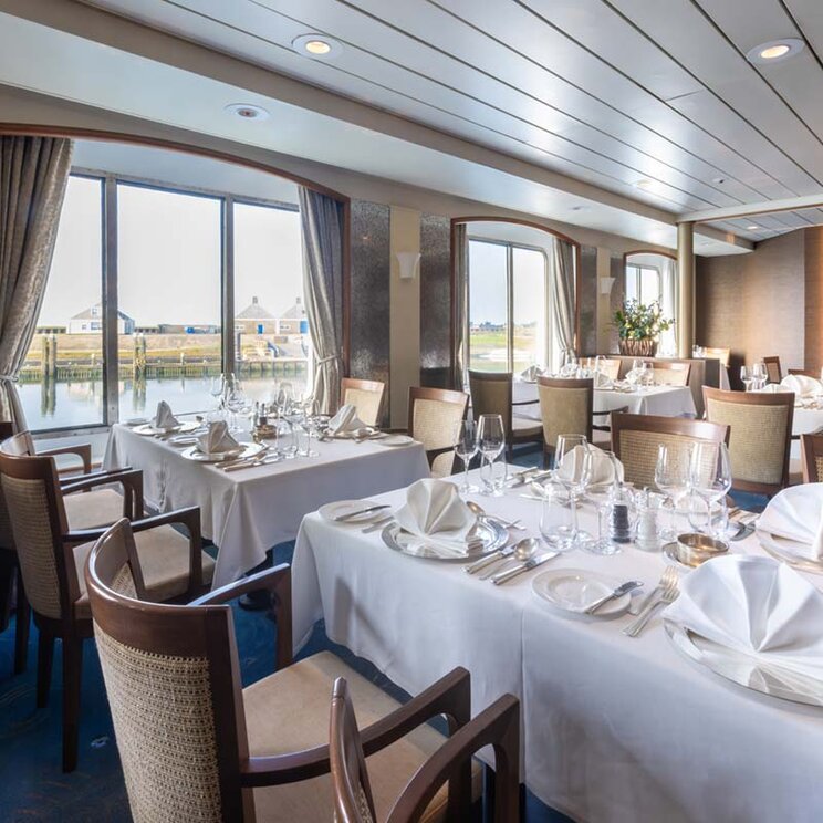 Restaurant an Bord der Ocean Seaventure Antarktis Expeditionskreuzfahrt mit weiß gedeckten Tischen, großen Fenstern und Blick nach draußen.