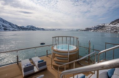 Das Außendeck der Ocean Albatros mit beheiztem Whirlpool und Liegen mit Blick auf das Wasser und schneebeckte Landschaft