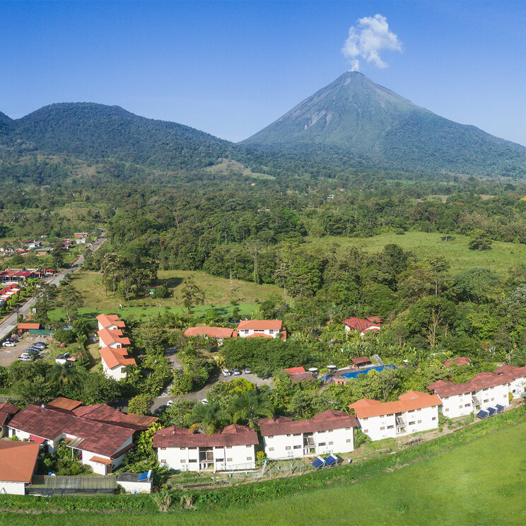 Drohnenaufnahme der weitläufigen Hotelanlage mit roten Dächern vor dem Vulkan Arenal in La Fortuna.