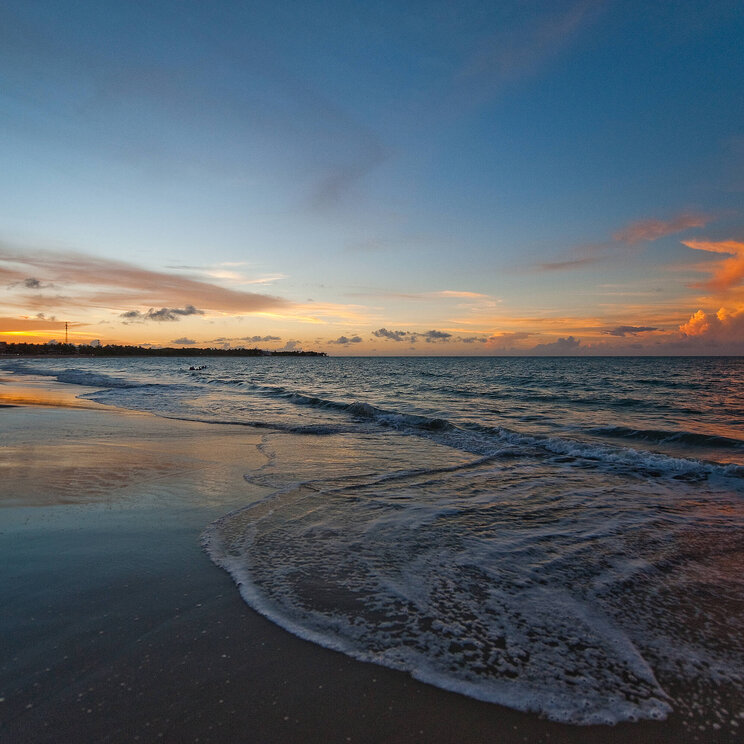 Strand von Cabarete in der Dominikanischen Republik bei Sonnenuntergang mit sanften Wellen und farbenfrohem Himmel.