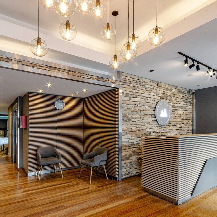 Moderne Rezeption im Hotel Alto Andino in Ushuaia, Argentinien, mit stilvollen Holzelementen, Steinwand, Designbeleuchtung und gemütlicher Sitzecke.