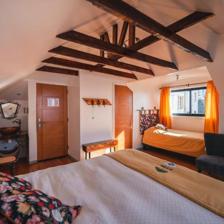 Hell eingerichtetes Zimmer mit Holzbalkendecke, Doppelbett und Einzelbett in Valparaiso.