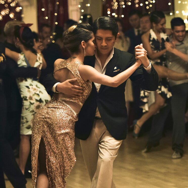 Ein Paar tanzt eng umschlungen Tango auf einer Milonga in Argentinien vor Lichterketten.
