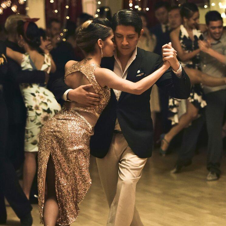Ein Paar tanzt eng umschlungen Tango auf einer Milonga in Argentinien vor Lichterketten.