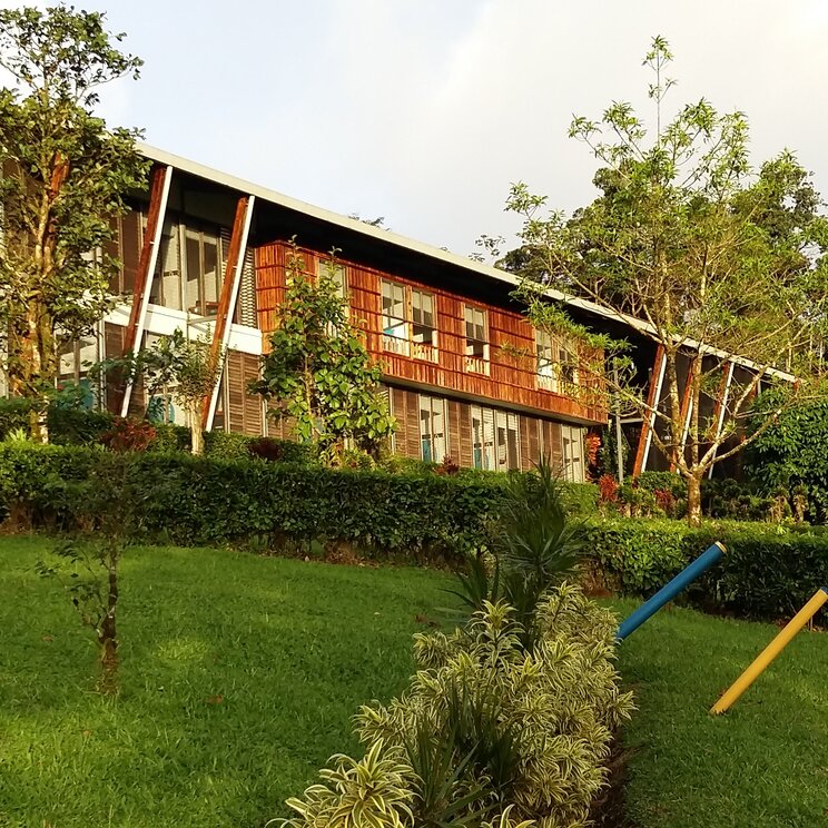 Zweistoeckiges Hauptgebaeude der Celeste Mountain Lodge in Costa Rica mit Holzfassade hinter einer gruenen Wiese.