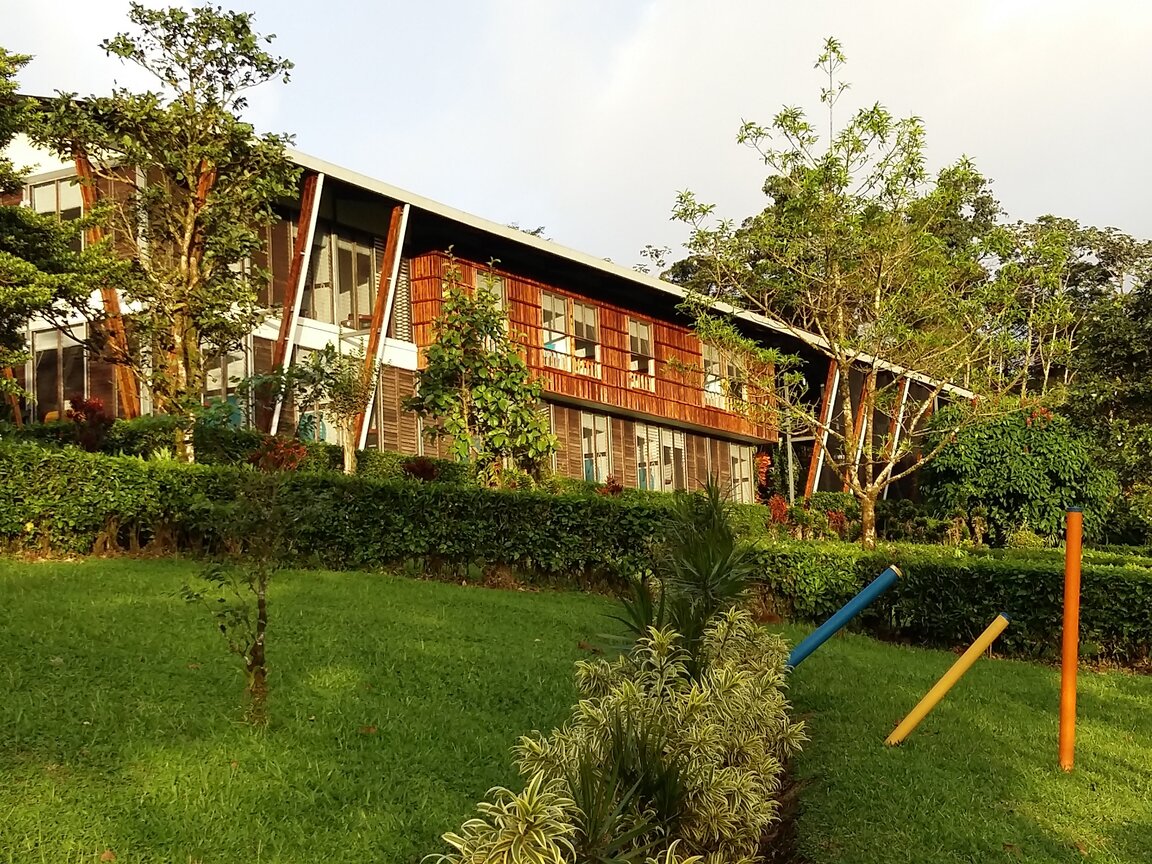 Zweistoeckiges Hauptgebaeude der Celeste Mountain Lodge in Costa Rica mit Holzfassade hinter einer gruenen Wiese.