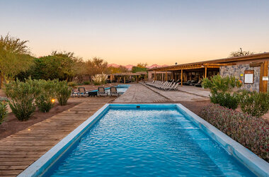 Hotel Cumbres San Pedro de Atacama: Länglicher Pool mit Holzsteg, Liegestühlen und Blick auf die Anden bei Sonnenuntergang.
