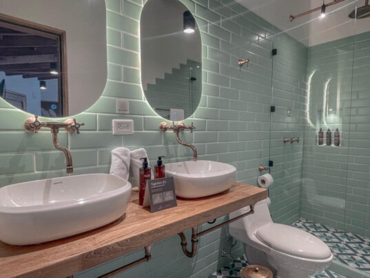 Modern gestaltetes Badezimmer im Masaya Collection Camelia in Bogotá, Kolumbien mit grünen Fliesen, Doppelwaschbecken, Regendusche und stimmungsvoller Beleuchtung.