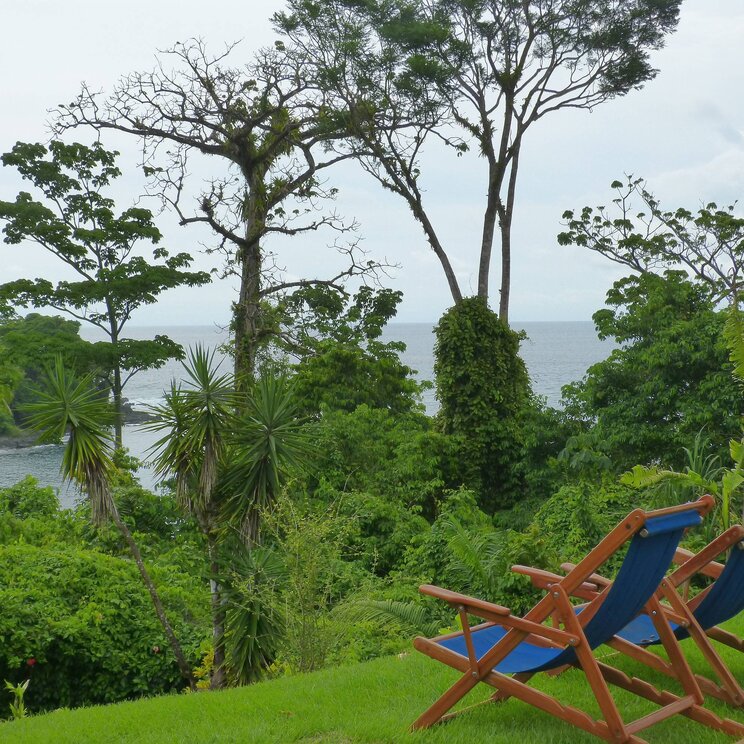 Blick auf den Ozean von der Las Caletas Lodge in Costa Rica, umgeben von grünen Pflanzen und zwei Liegestühlen im Vordergrund.