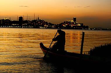Fischer im Sonnenuntergang mit Küstenlandschaft im Hintergrund
