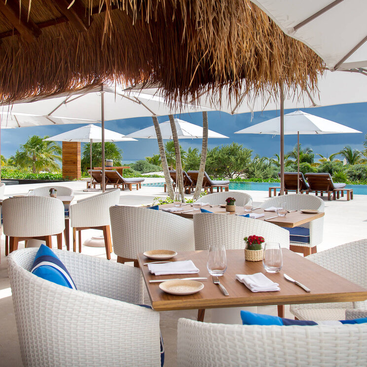Restaurantterrasse im Hotel Chablé Maroma in Punta Maroma, Mexiko, mit stilvollen Sitzmöbeln, Blick auf den Pool und tropischer Umgebung unter weißen Sonnenschirmen.