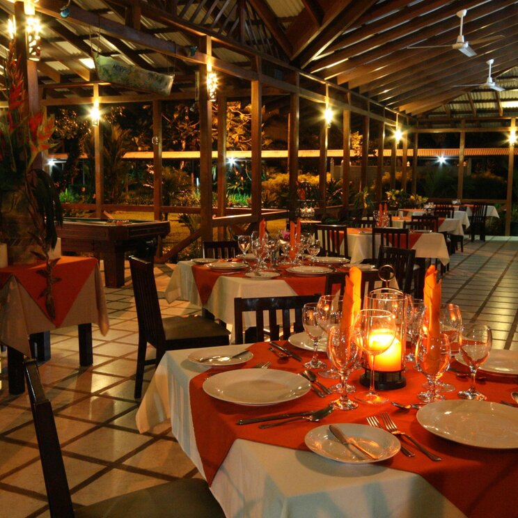 Restaurant im Manatus Hotel in Tortuguero, Costa Rica, mit stilvoll gedeckten Tischen und abendlicher Beleuchtung.