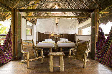 Schlafzimmer mit zwei Betten, Moskitonetzen, Holzstuehlen und Haengematten in Puerto Maldonado, Peru.