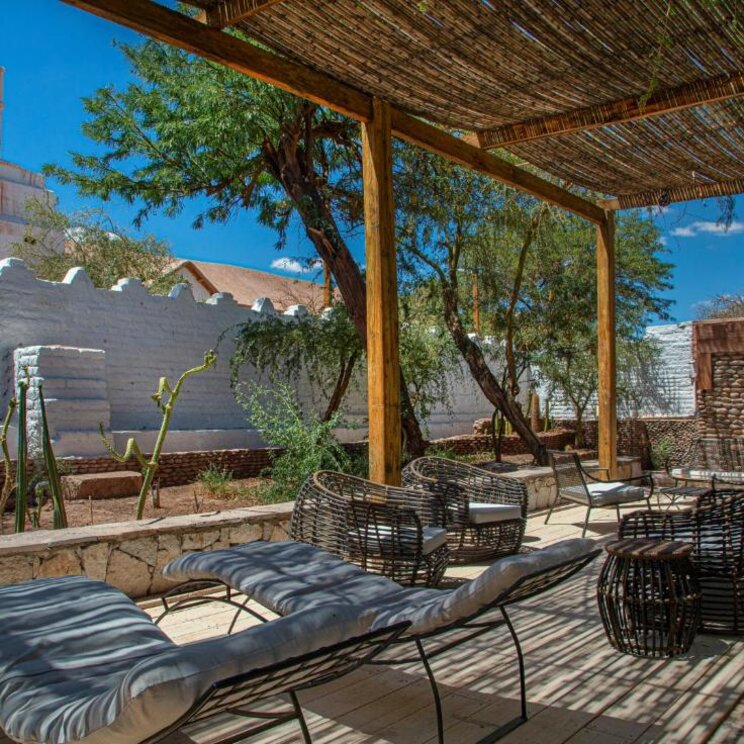 Überdachte Terrasse mit Korbsesseln, Liegen und Blick auf eine weisse Kirche in der Atacama Wüste, Chile.