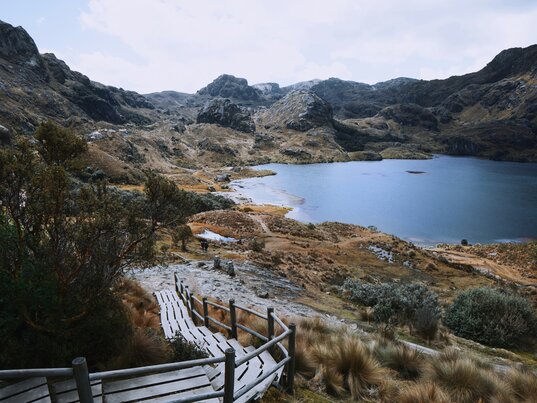 Eine tiefblaue Lagune im Cajas-Nationalpark in Ecuador, umgeben von schroffen Berghängen und typischer Páramo-Vegetation unter dramatischen Wolken.