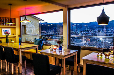 Restauranttische an grossen Fenstern mit Panoramablick ueber die Daechre von Cusco bei Daemmerung.