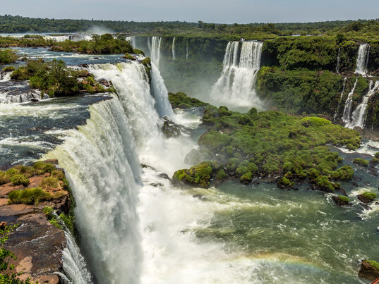 Panorama der Iguazú-Wasserfälle mit herabstürzenden Wassermassen und grüner Vegetation in Foz do Iguaçu, Brasilien.