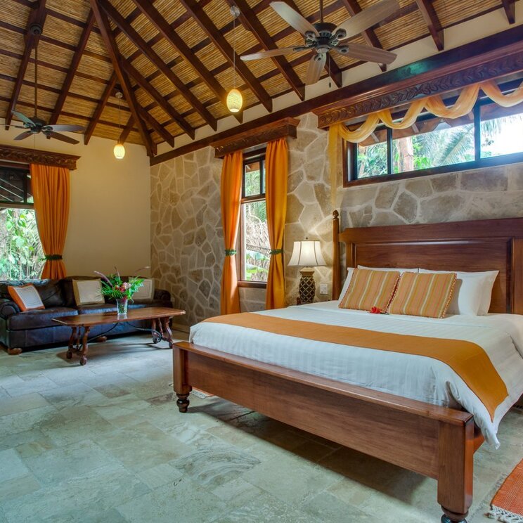 Schlafzimmer im Creekside Cottage mit Holzbalkendecke, Steinwand und Doppelbett in San Ignacio, Belize.