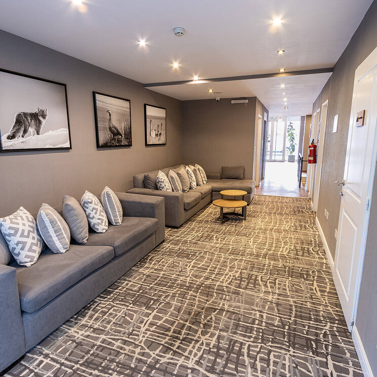 Loungebereich im Hotel Alto Andino in Ushuaia, Argentinien, mit modernen Sofas, dekorativen Schwarz-Weiß-Fotografien und stilvollem Teppichdesign im Flur.