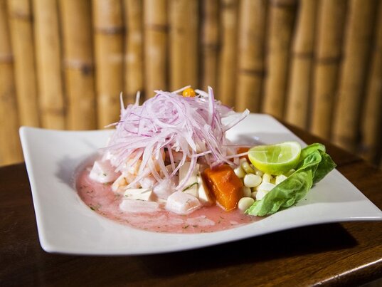Peruanisches Ceviche mit roten Zwiebeln, Mais, Süßkartoffel und Limette in einer weißen Schale.