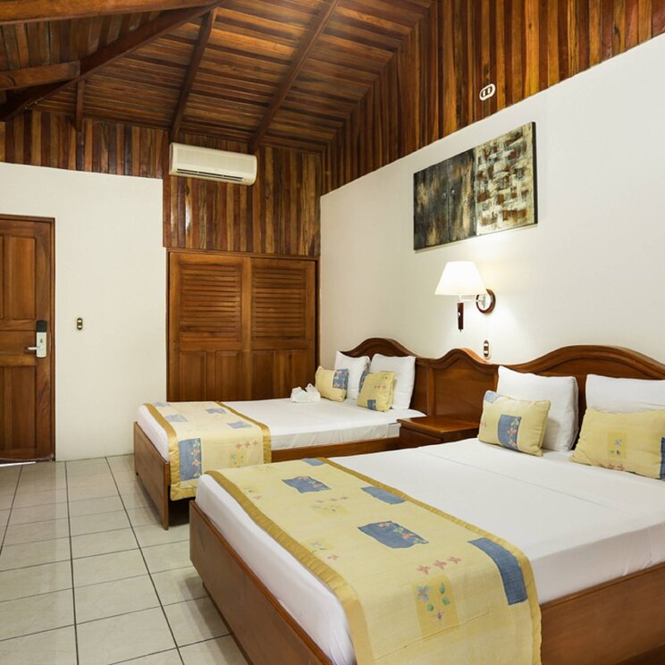 Standardzimmer im Hotel Arenal Paraíso Resort & Spa in La Fortuna, Costa Rica, mit zwei Doppelbetten, Holzmöbeln und Decke im Landhausstil.