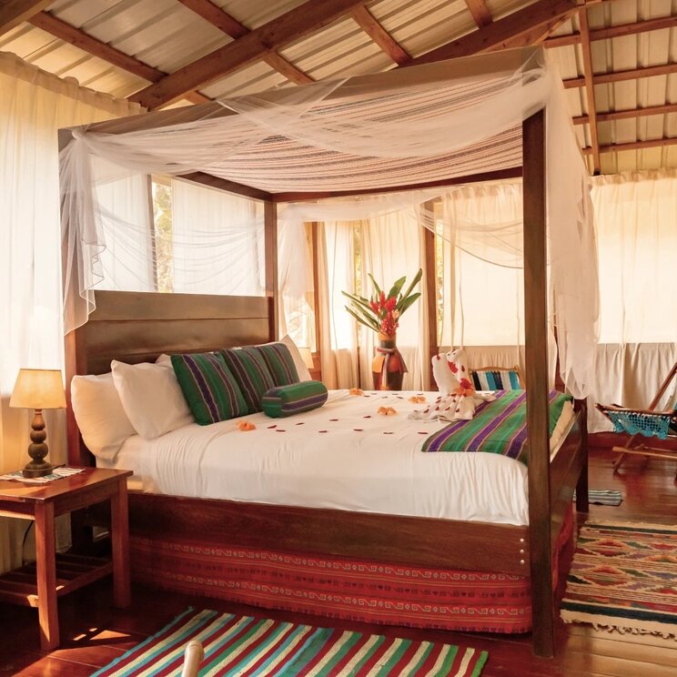 Schlafzimmer mit großem hölzernen Himmelbett, bunten Läufern und Moskitonetz in San Ignacio, Belize.
