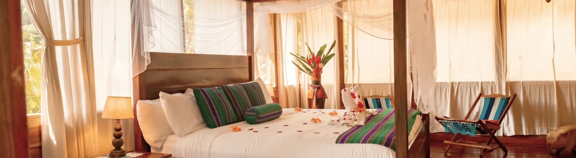 Schlafzimmer mit großem hölzernen Himmelbett, bunten Läufern und Moskitonetz in San Ignacio, Belize.