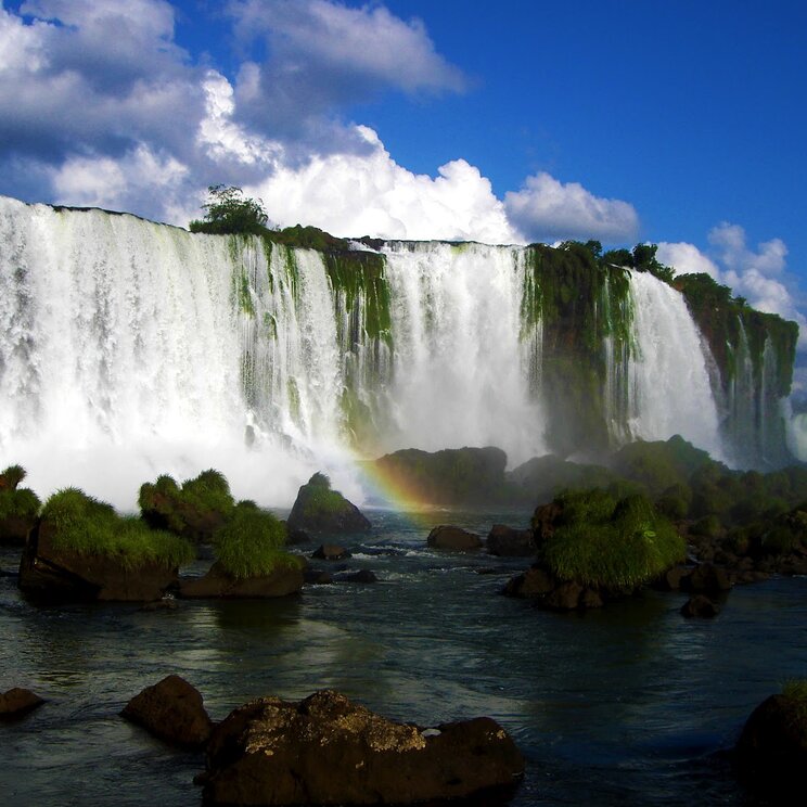 Die beeindruckenden Iguazú-Wasserfälle mit Regenbogen und umgeben von Dschungel.