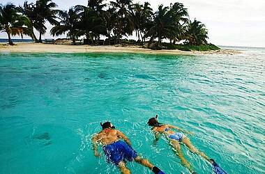 Zwei Personen schnorcheln im türkisfarbenen Wasser direkt vor einer Insel in Belize