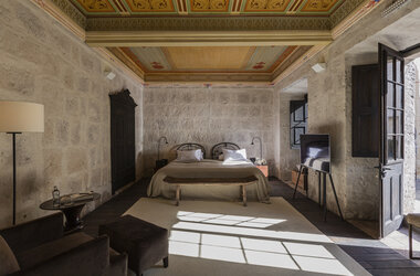 Hotelzimmer mit historisch bemalter Holzdecke, Sillar-Steinwaenden und Doppelbett im CIRQA Arequipa.